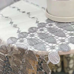 Nappe élégante avec motifs brodés gris et détails ajourés, ornant superbement une table pour un look raffiné et sophistiqué. Idéale pour décorer et rehausser l'esthétique de votre salle à manger ou espace réception.