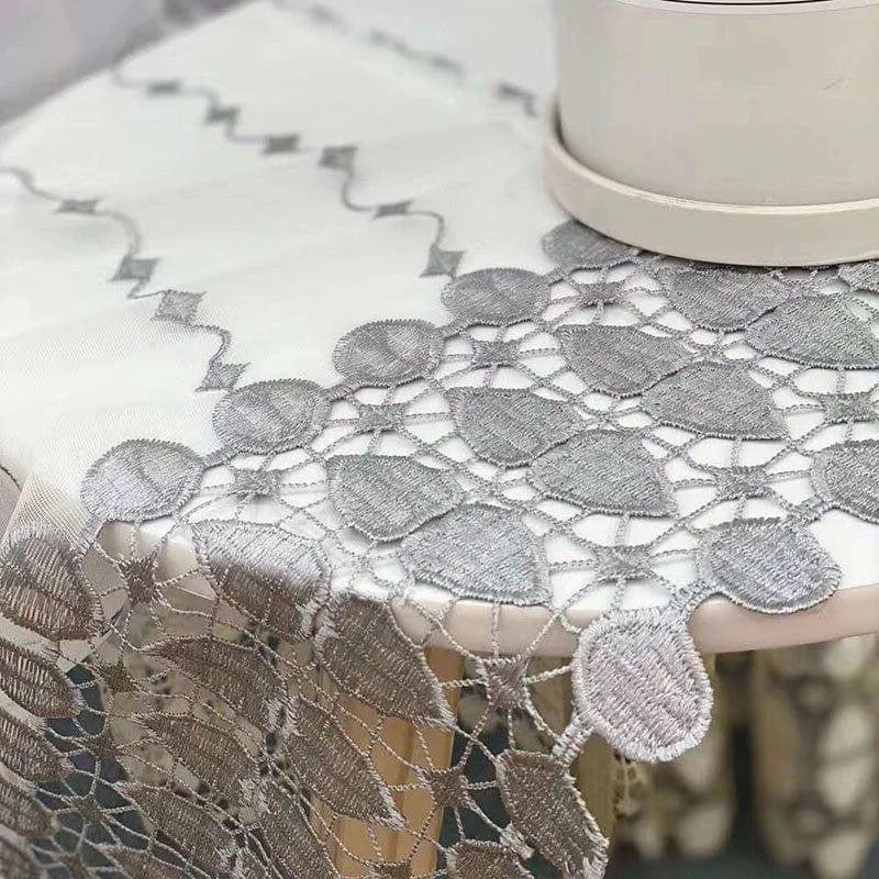 Nappe élégante avec motifs brodés gris et détails ajourés, ornant superbement une table pour un look raffiné et sophistiqué. Idéale pour décorer et rehausser l'esthétique de votre salle à manger ou espace réception.