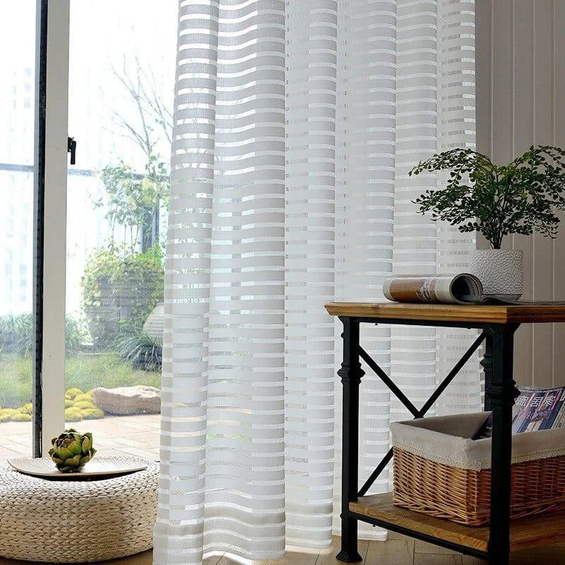 Élégant rideau blanc à rayures verticales pour un salon moderne. Ce modèle apporte luminosité et intimité à votre intérieur. Idéal pour les grandes baies vitrées, il complète parfaitement une décoration contemporaine. Accessoirisé avec une table en bois, une plante verte et un magazine pour une touche naturelle et accueillante.