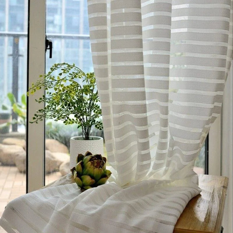 Voilage à rayures blanches filtrant la lumière, idéal pour un salon moderne avec vue sur le balcon. Élégant et pratique, il met en valeur vos plantes d'intérieur tout en créant une ambiance lumineuse.