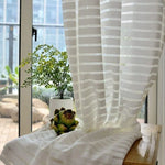 Voilage à rayures blanches filtrant la lumière, idéal pour un salon moderne avec vue sur le balcon. Élégant et pratique, il met en valeur vos plantes d'intérieur tout en créant une ambiance lumineuse.