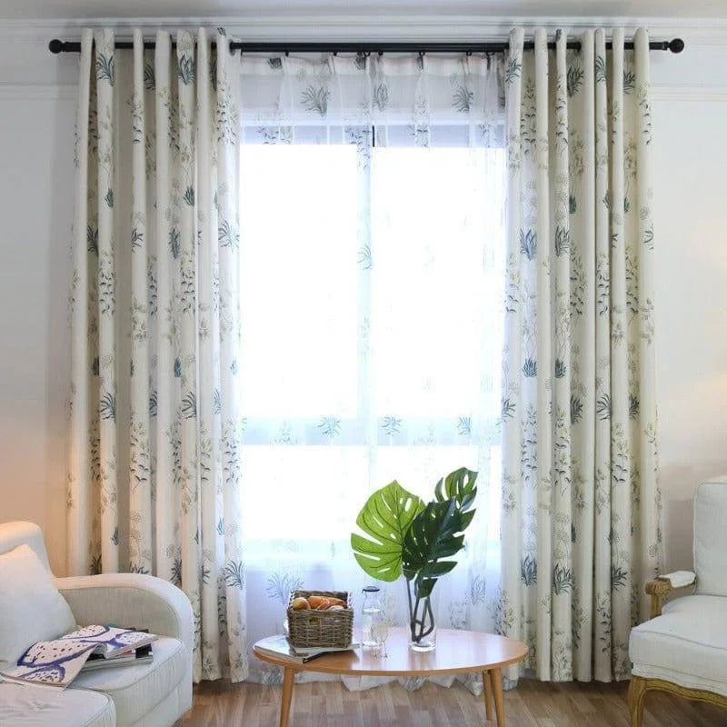 Rideaux élégants à motifs floraux dans un salon lumineux, encadrant une fenêtre avec voilage translucide. Ambiance apaisante propice à la détente, avec un canapé confortable, une table basse en bois décorée de feuilles vertes et un panier de fruits. Décoration intérieure moderne et nature, idéale pour créer une atmosphère chaleureuse et accueillante.
