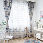 Rideaux élégants à motif de poissons bleus, apportant une touche marine et moderne à la décoration intérieure. Accent parfait pour une ambiance lumineuse et aérée dans une chambre d’enfant ou un salon, avec un fauteuil à bascule en bois et un bureau blanc complétant l’ensemble du décor épuré.