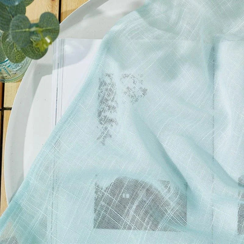 Voilage turquoise léger drapé sur une table en bois, avec une plante verte en décoration. Idéal pour ajouter une touche de fraîcheur et de douceur à votre intérieur. Accessoire décoratif moderne et élégant.