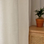 Rideau blanc à motif géométrique moderne, parfait pour ajouter une touche d'élégance à votre intérieur. Ce rideau s'harmonise parfaitement avec une décoration végétale et un mobilier en bois, créant une ambiance chaleureuse et apaisante dans votre salon ou chambre.