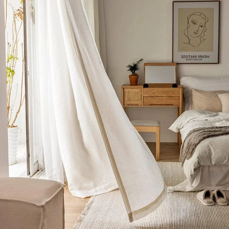 Chambre élégante avec décoration moderne et épurée, rideaux blancs fluides laissant entrer la lumière naturelle, mobilier en bois clair, literie confortable, tapis texturé beige, ambiance apaisante et harmonieuse idéale pour un intérieur chaleureux et accueillant.