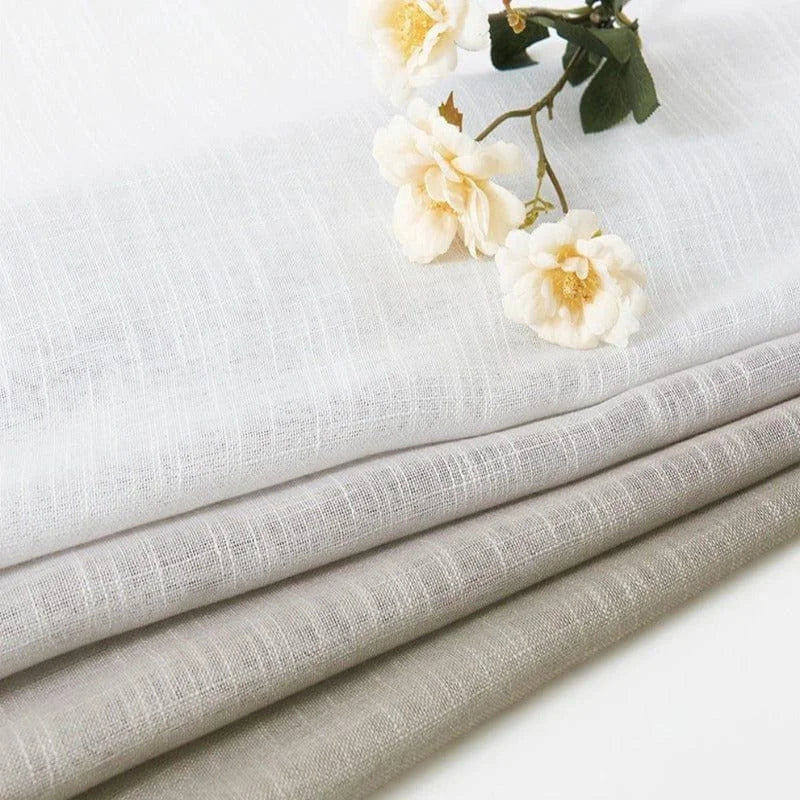 Tissus élégants de couleur blanche et grise, soigneusement pliés, accompagnés de fleurs délicates, parfaits pour la décoration intérieure. Adaptés à la confection de rideaux ou d'éléments textiles décoratifs, ces tissus apportent une touche de raffinement à n'importe quel espace. Idéal pour créer une ambiance chaleureuse et apaisante dans votre maison.