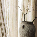 Vase décoratif en pierre grise avec branches sèches en arrière-plan de rideaux beiges à rayures, ajoutant une touche naturelle et élégante à tout intérieur moderne. Parfait pour un séjour raffiné ou un espace de vie minimaliste.
