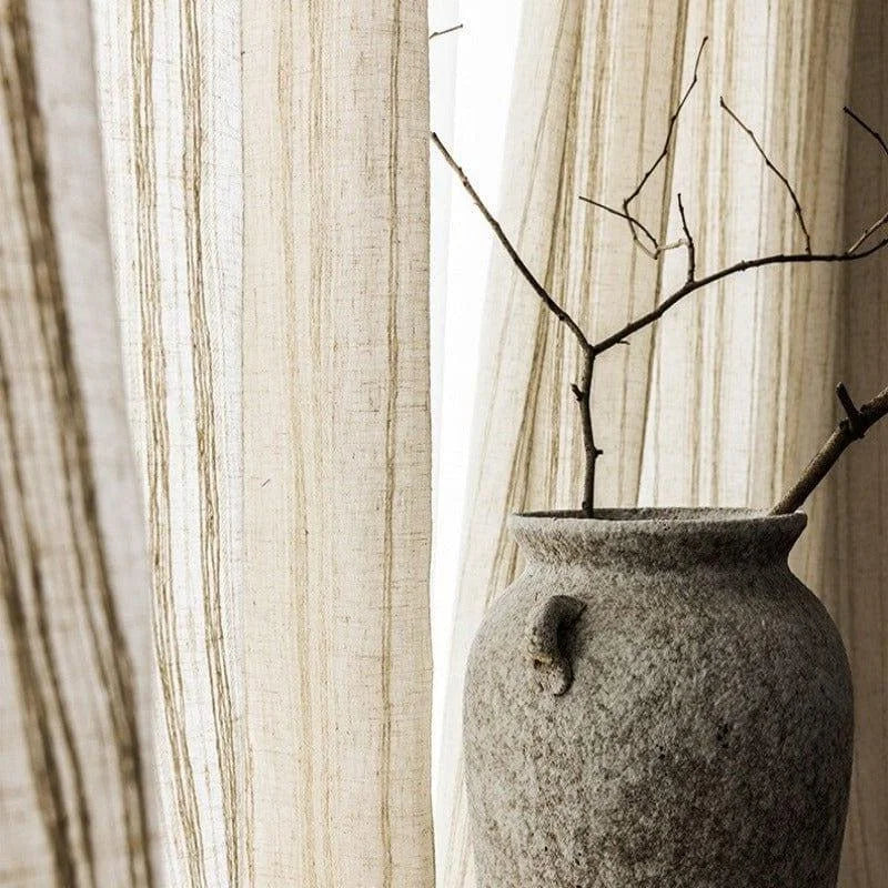 Vase décoratif en pierre grise avec branches sèches en arrière-plan de rideaux beiges à rayures, ajoutant une touche naturelle et élégante à tout intérieur moderne. Parfait pour un séjour raffiné ou un espace de vie minimaliste.