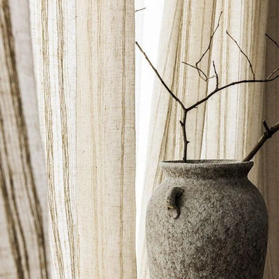 Vase décoratif en pierre grise avec branches sèches en arrière-plan de rideaux beiges à rayures, ajoutant une touche naturelle et élégante à tout intérieur moderne. Parfait pour un séjour raffiné ou un espace de vie minimaliste.