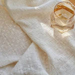 Tissu blanc texturé avec motif géométrique délicat, accompagné d'un verre facetté élégant, idéal pour décorer et embellir votre espace de vie avec une touche de raffinement.