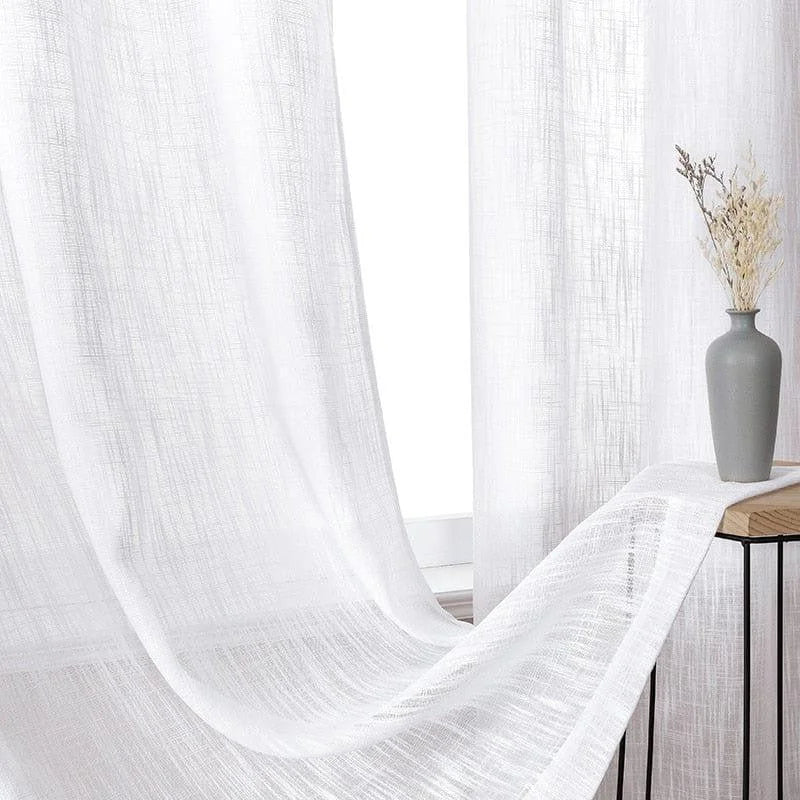 Voilage blanc élégant drapé près d'une fenêtre, apportant luminosité et douceur à la pièce, avec un vase décoratif contenant des branches sèches pour une touche naturelle et moderne. Idéal pour une décoration intérieure épurée et chaleureuse.