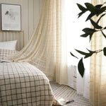 Chambre lumineuse et élégante avec lit au design moderne, parure à carreaux, rideaux ajourés, et détails déco apaisants. Idéal pour créer une ambiance cosy et raffinée. Présence de lumière naturelle et de plantes pour une atmosphère sereine.