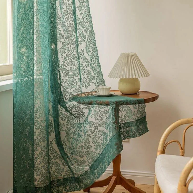 Rideau décoratif vert à motif floral, parfait pour apporter une touche élégante et sophistiquée à n'importe quel intérieur. Installé dans une pièce lumineuse, il est posé près d'une petite table en bois sur laquelle reposent une lampe de chevet au design moderne et une tasse. Ce rideau est idéal pour créer une atmosphère chaleureuse et accueillante dans le salon ou la chambre.