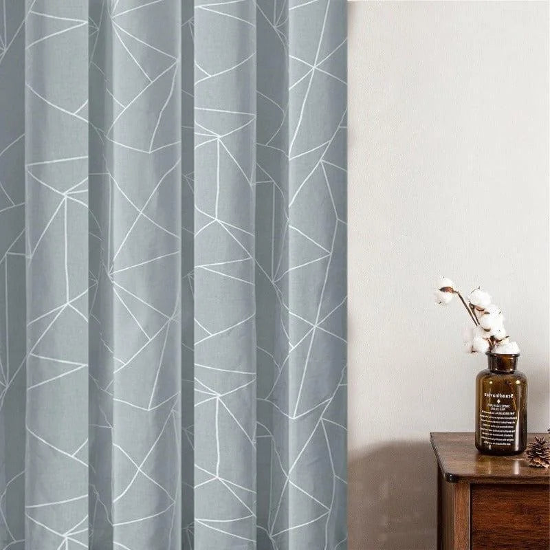 Rideau gris avec motifs géométriques modernes, idéal pour une décoration intérieure élégante et contemporaine, présenté à côté d'une table en bois avec un vase décoratif.