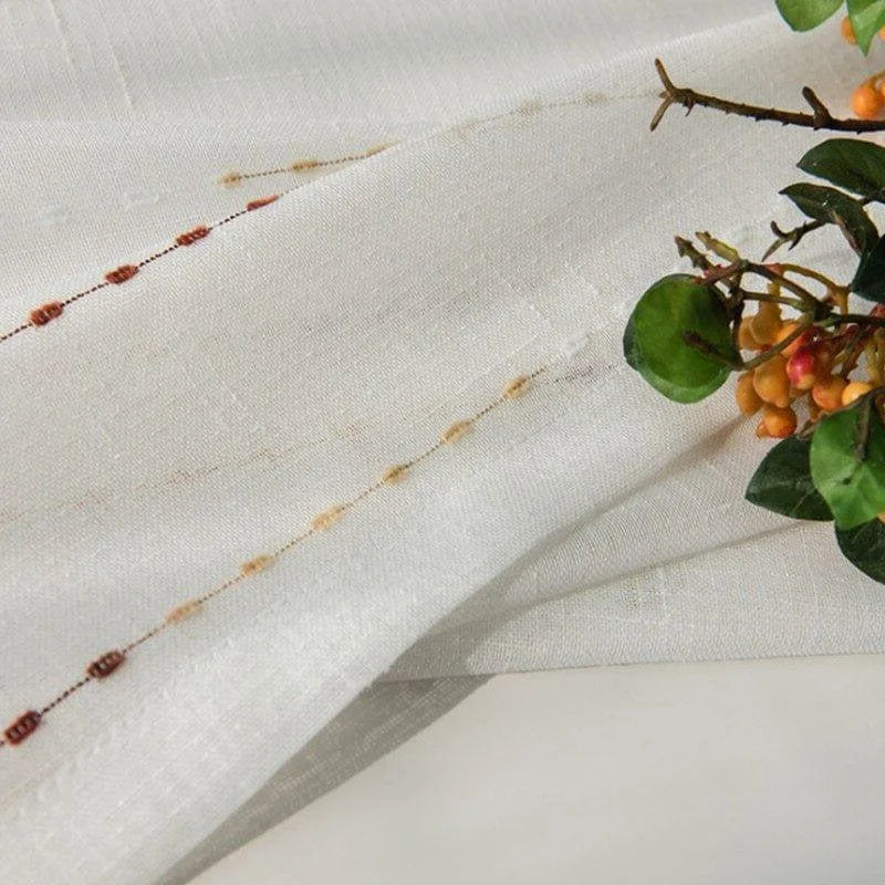 Image montrant un élégant tissu blanc orné de délicates broderies colorées, parfait pour la décoration intérieure. Les motifs ajoutent une touche de sophistication et de charme à tout espace. Idéal pour les rideaux ou les nappes, ce design apporte une ambiance chaleureuse et accueillante.