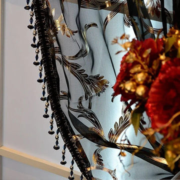 Rideau décoratif avec motifs floraux noirs et dorés, agrémenté de perles suspendues, idéal pour ajouter une touche d'élégance et de sophistication à votre intérieur. Les motifs raffinés fusionnent harmonieusement avec un joli bouquet de fleurs rouges, créant une ambiance chaleureuse et luxueuse dans la pièce. Parfait pour embellir salons et chambres avec style et charme.