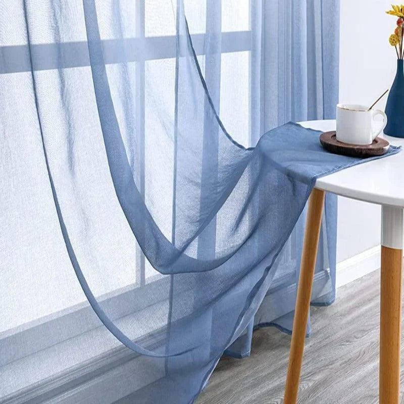 Voilage bleu léger et élégant décorant une fenêtre moderne, laissant entrer la douce lumière naturelle. Parfaits pour ajouter une touche de sophistication à tout salon ou chambre, ces rideaux créent une atmosphère apaisante et raffinée dans votre intérieur.