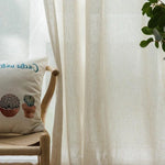 Coussin décoratif avec motifs de cactus sur chaise en bois clair, accompagné de rideaux clairs laissant passer une lumière douce, parfait pour une ambiance intérieure naturelle et apaisante. Ce design élégant s'intègre harmonieusement dans un salon ou une chambre, ajoutant une touche de nature et de style contemporain.
