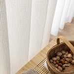 Rideaux à motifs géométriques élégants pour la décoration intérieure, présents dans un espace de vie éclairé par la lumière naturelle ambiante. À côté, un panier en osier contenant des éléments décoratifs naturels, idéal pour ajouter une touche rustique à votre maison. Solution parfaite pour embellir votre intérieur et créer une atmosphère cosy.