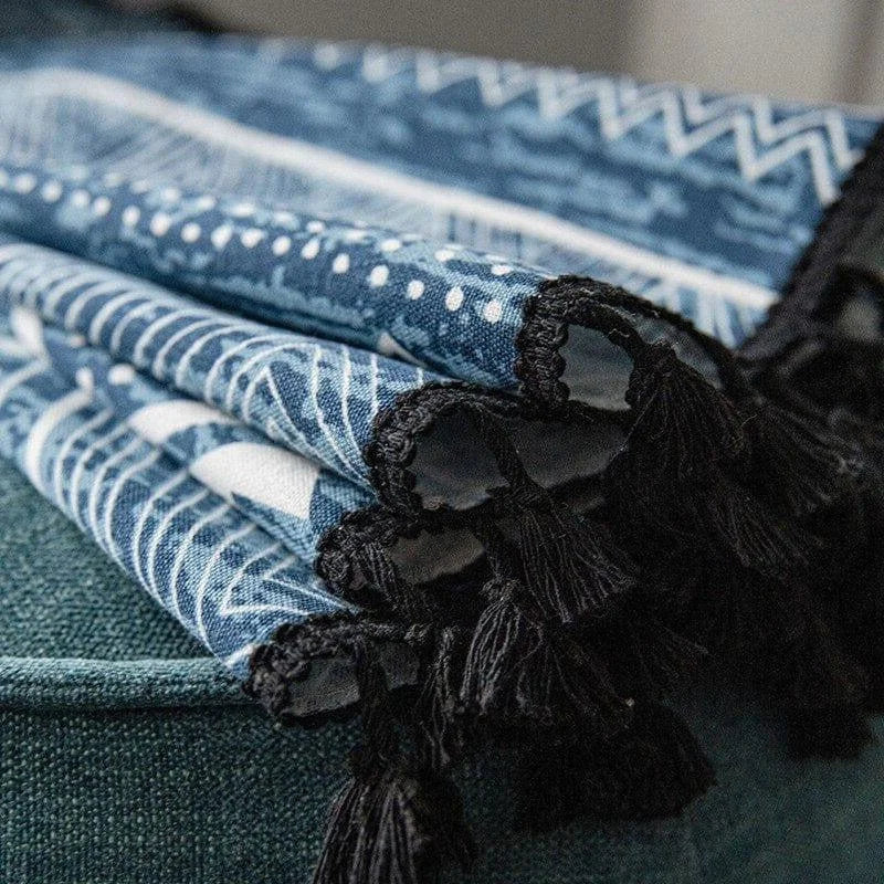 Plaid bleu avec motifs géométriques blancs, bordé de franges noires élégantes. Ce jeté ajoute une touche bohème et chic à votre intérieur, idéal pour le salon ou la chambre. Accessoire déco parfait pour un style tendance.