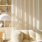 Salon moderne avec canapé confortable et lampe design, décoré avec des rideaux légers laissant passer la lumière naturelle. Espace de vie élégant et doux, avec des accessoires décoratifs sur une étagère. Idéal pour créer une ambiance chaleureuse et accueillante.