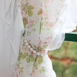 Rideau floral romantique avec motif de roses et feuillage vert, retenu par un embrasse perlé élégant, idéal pour ajouter une touche de charme vintage à votre intérieur.