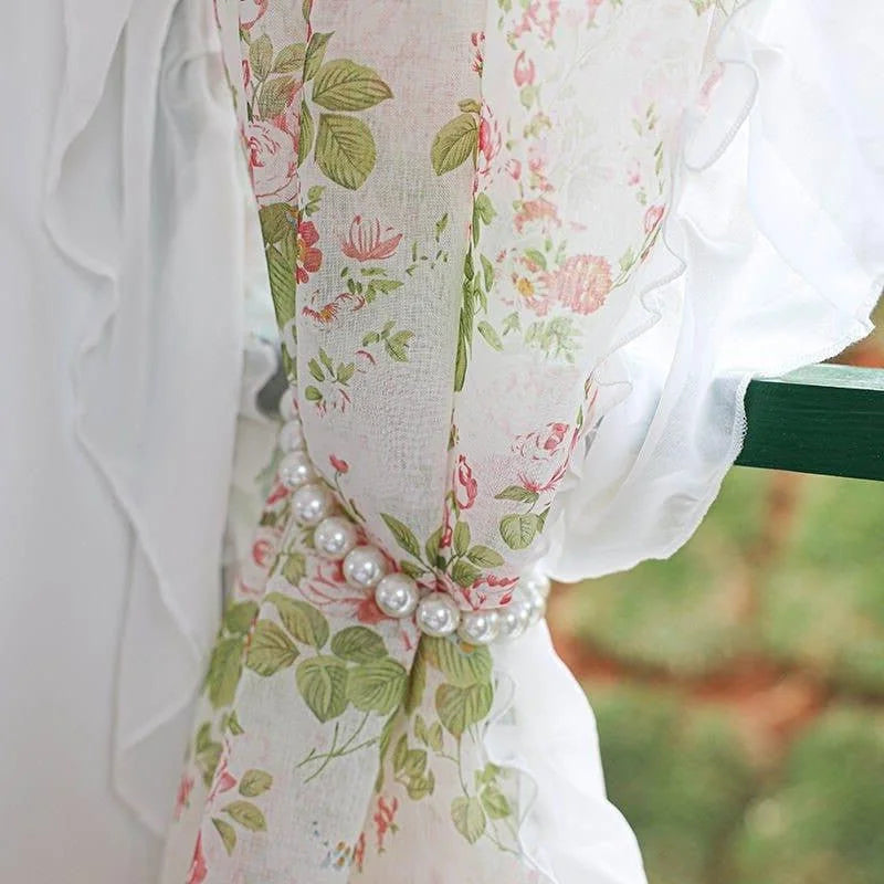 Rideau floral romantique avec motif de roses et feuillage vert, retenu par un embrasse perlé élégant, idéal pour ajouter une touche de charme vintage à votre intérieur.