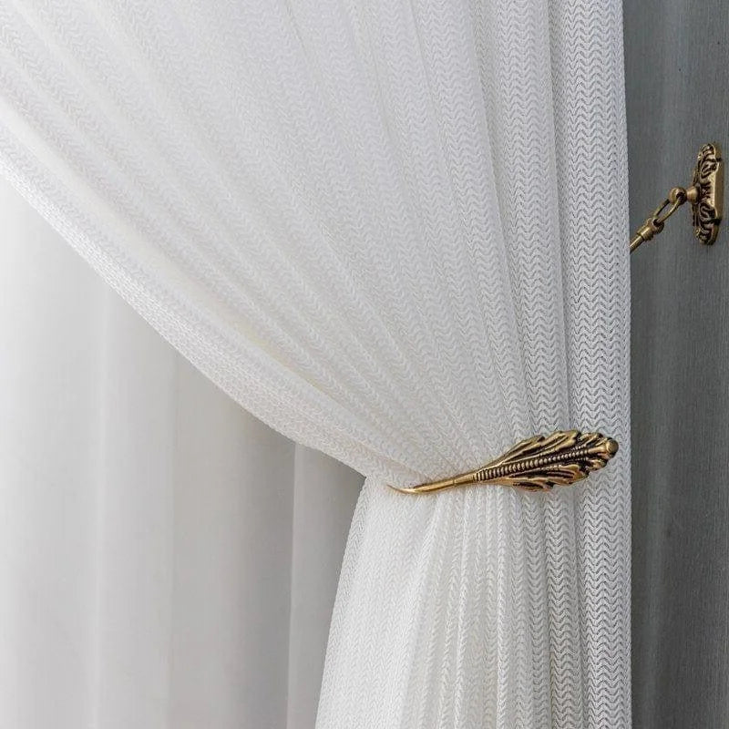 Rideau blanc élégant avec motif discret, maintenu par un embrasse métallique dorée décorative en forme de feuille, apportant une touche de raffinement et de sophistication à votre intérieur. Parfait pour un salon ou une chambre à coucher moderne, ce rideau combine esthétique et fonctionnalité pour une décoration intérieure harmonieuse.