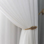 Rideau blanc élégant avec motif discret, maintenu par un embrasse métallique dorée décorative en forme de feuille, apportant une touche de raffinement et de sophistication à votre intérieur. Parfait pour un salon ou une chambre à coucher moderne, ce rideau combine esthétique et fonctionnalité pour une décoration intérieure harmonieuse.
