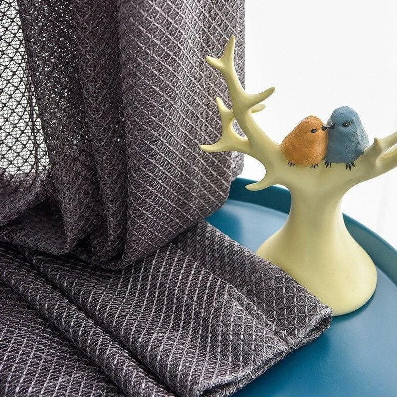 Rideau décoratif gris avec motif texturé, mis en valeur sur une table bleu canard, accompagné d'un élégant porte-bijoux en forme de branche, accueillant deux oiseaux colorés. Parfait pour ajouter une touche d'élégance et de modernité à votre intérieur. Ideal pour le salon ou la chambre.