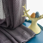 Rideau décoratif gris avec motif texturé, mis en valeur sur une table bleu canard, accompagné d'un élégant porte-bijoux en forme de branche, accueillant deux oiseaux colorés. Parfait pour ajouter une touche d'élégance et de modernité à votre intérieur. Ideal pour le salon ou la chambre.