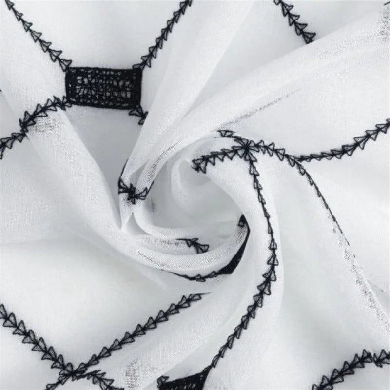 Tissu décoratif blanc avec motifs géométriques noirs, idéal pour la confection de vêtements ou la décoration intérieure, offrant un style moderne et élégant.
