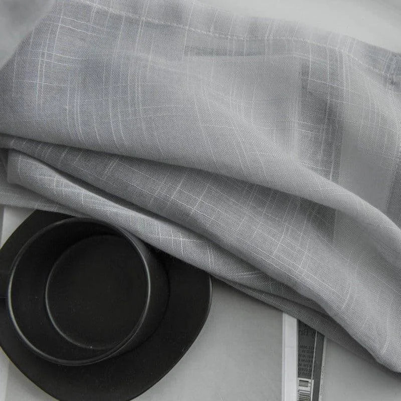Voilage gris élégant avec motifs texturés, idéal pour apporter une touche moderne et lumineuse à votre intérieur. Convient parfaitement aux salons ou chambres contemporaines. Accessoirisé avec une vaisselle noire design pour un contraste chic et minimaliste.