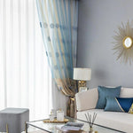 Salon moderne et élégant avec des rideaux bleus décoratifs, un canapé blanc agrémenté de coussins bleus, une table basse en verre ornée d'accessoires sophistiqués, et une lampe de table raffinée, créant une atmosphère chic et apaisante. Décoration murale en forme de soleil doré apportant une touche de style unique.