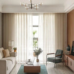 Salon moderne avec un canapé confortable et fauteuil élégant face à une table basse design. Rideaux en fond pour un éclairage naturel optimal. Décoration intérieure épurée avec plantes et accessoires modernes, créant une ambiance chaleureuse et accueillante. Lustre chic pour une touche d'élégance. Idéal pour des inspirations déco actuelles.