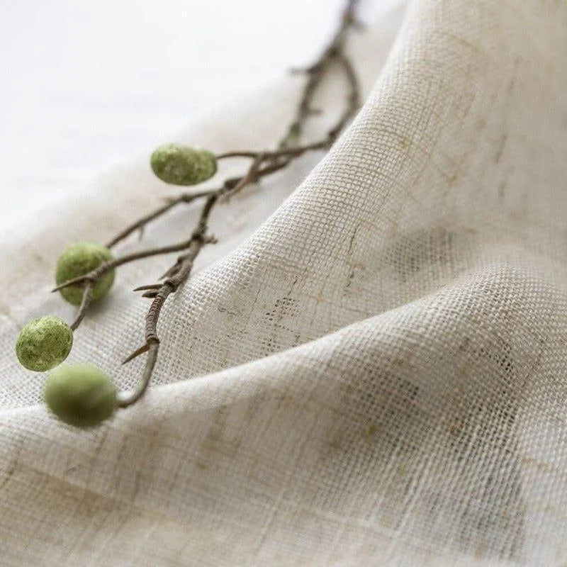 Image d'un tissu naturel drapé, accentué par une branche avec des baies vertes, créant une ambiance végétale et organique. Ce produit est parfait pour une décoration intérieure inspirée par la nature.