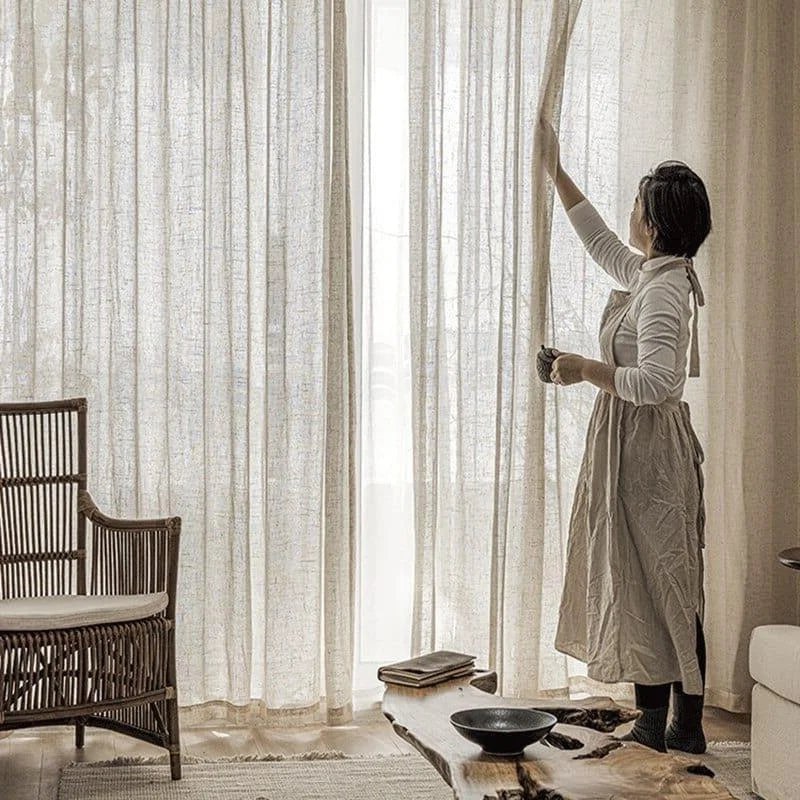 Rideaux élégants pour salon illuminé, idéals pour une décoration intérieure chaleureuse. Femme ajustant les rideaux pour optimiser la lumière naturelle. Ambiance cosy et moderne avec fauteuil en rotin et table basse en bois. Parfait pour créer une atmosphère accueillante dans le salon.