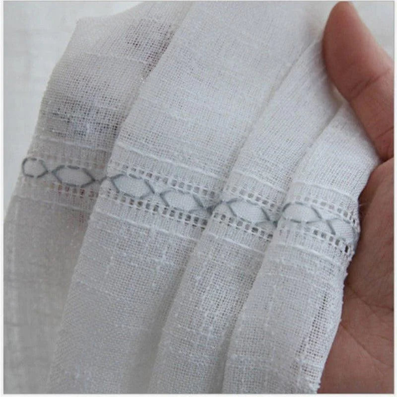 Tissu translucide blanc avec motifs géométriques, tenu dans une main. élégant et léger, idéal pour la décoration intérieure ou la confection de vêtements.