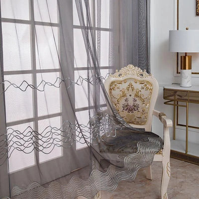 Voilage décoratif gris élégant pour salon avec motifs ondulés, accompagnant un fauteuil classique au design floral. Idéal pour une décoration intérieure raffinée, créant une ambiance lumineuse et sophistiquée.