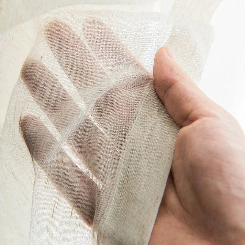 Main tenant délicatement un tissu léger et translucide, idéal pour la confection de vêtements aérés ou de rideaux élégants. Translucidité et finesse pour une allure raffinée et moderne.