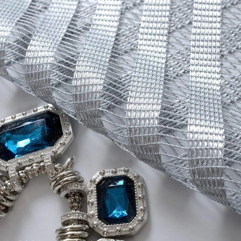 Broderie argentée élégante avec ornements bleus. Conception raffinée idéale pour décorer des vêtements ou accessoires de mode. Détail de perle bleue centrale entourée d'éléments argentés qui captent la lumière. Parfait pour ajouter une touche de luxe et de sophistication à vos créations.