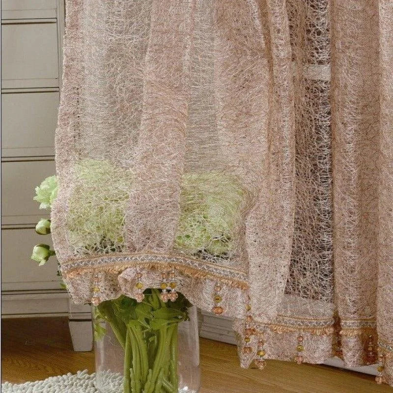 Rideau décoratif beige translucide avec ornements en perles suspendu dans un salon élégant. Ce voile ajoute une touche raffinée et chaleureuse à la pièce, parfait pour créer une ambiance intime et accueillante. Idéal pour un design intérieur chic et contemporain.
