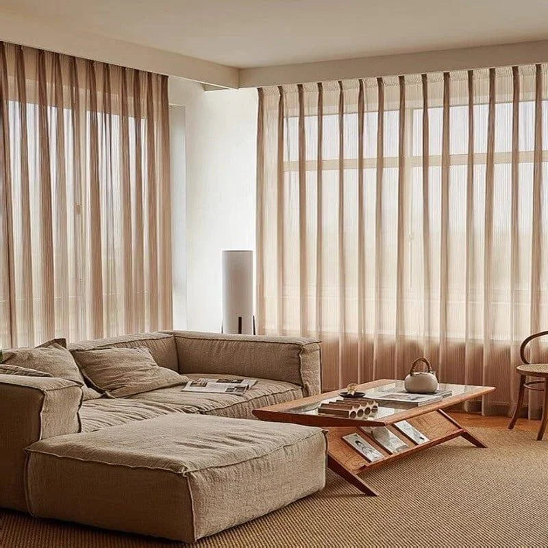 Salon contemporain avec un canapé d'angle confortable, décoré dans des tons neutres. Grande baie vitrée munie de rideaux légers, apportant luminosité et élégance. Table basse en bois au design moderne, parfait pour un intérieur chaleureux et accueillant. Atmosphère sereine et raffinée.