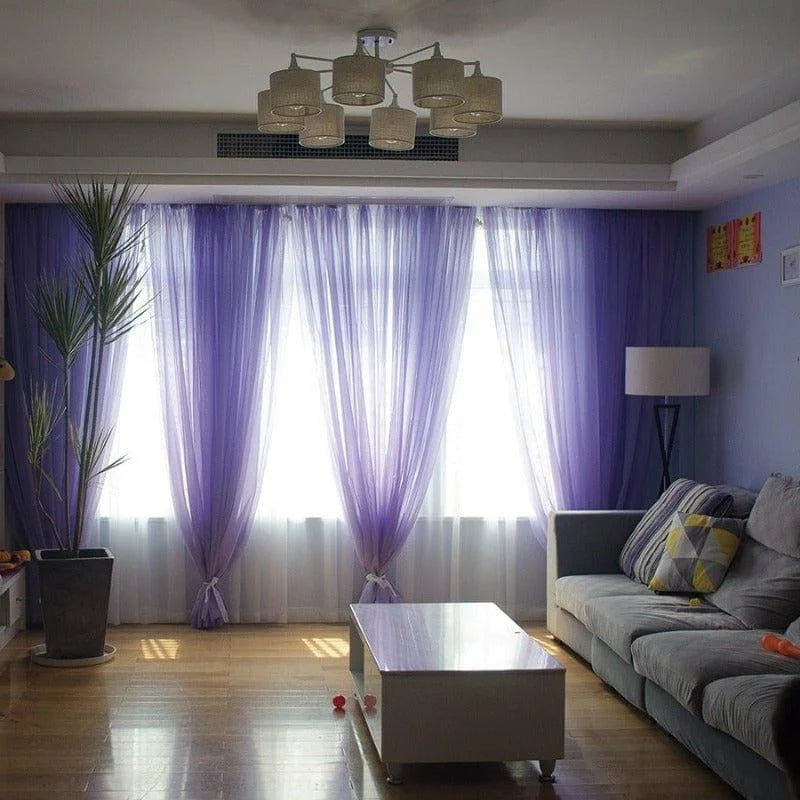 Salle de séjour moderne avec rideaux violets, canapé confortable, table basse élégante, éclairage suspendu design, et décoration intérieure raffinée.