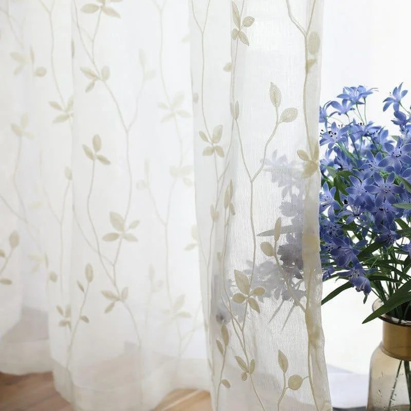Voilage décoratif avec motifs de feuilles, parfait pour embellir une fenêtre tout en laissant passer la lumière naturelle. Design élégant et raffiné, idéal pour apporter une touche de nature à votre intérieur. Convient parfaitement pour un salon, une chambre ou une salle à manger. Complément harmonieux avec des fleurs en vase pour une décoration intérieure apaisante et sophistiquée.