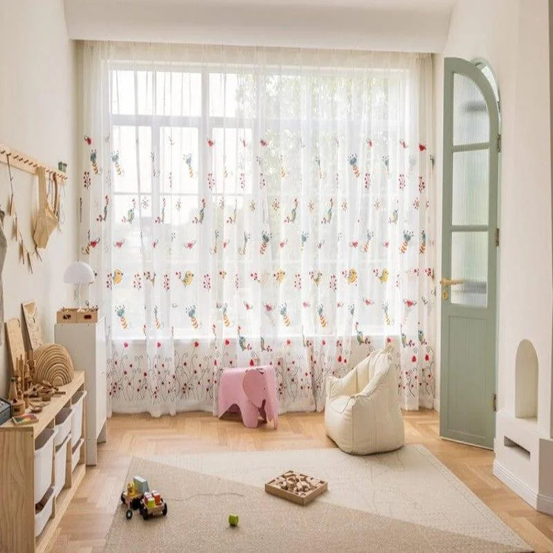 Chambre d'enfant lumineuse avec rideaux brodés de motifs colorés. Aménagement accueillant avec tapis doux, jouets en bois et décorations ludiques. Idéale pour créer un environnement chaleureux et stimulant.