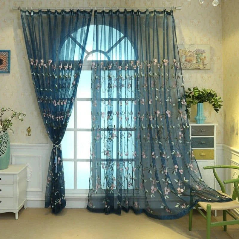 Rideau transparent bleu avec motifs floraux roses et verts, ornant élégamment une fenêtre arquée. Décoration intérieure chic, parfaite pour apporter une touche de nature et de sophistication à tout salon ou chambre à coucher. Accessible et délicat, ce rideau transforme l'atmosphère en un espace serein et accueillant.