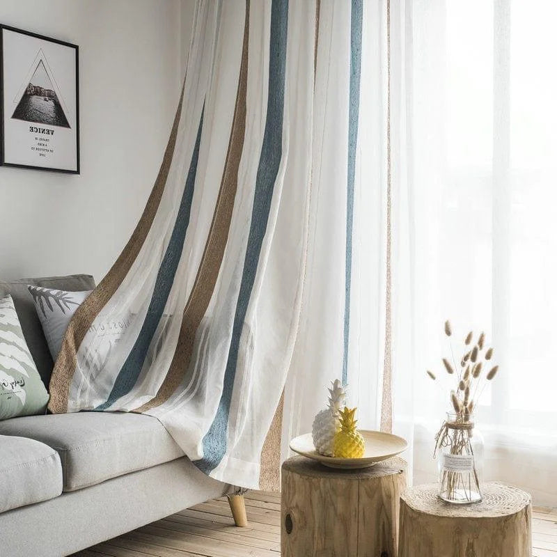 Rideaux modernes à rayures verticales bleues et beiges dans un salon lumineux. Décoration intérieure chic avec canapé gris, coussins à motifs, et table en bois rustique. Accessoires tendance avec ananas décoratif et vase en verre. Ambiance cosy et élégante pour un espace de vie contemporain.