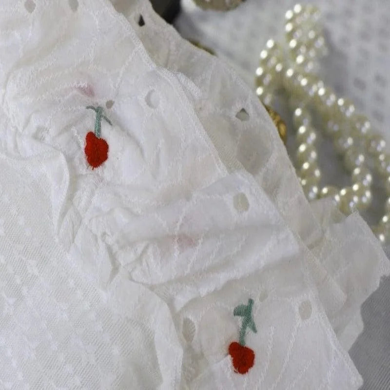 Gros plan sur un tissu délicat avec des petites broderies rouges représentant des fleurs sur un fond blanc. Parfait pour des créations textiles raffinées et élégantes. Arrière-plan avec des perles floues. Idéal pour les amateurs de couture et de mode en quête d’originalité et de style romantique.